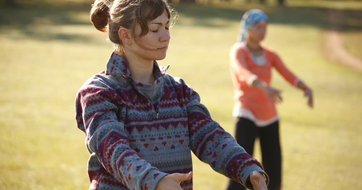 Woman practising mindful movement outdoors during a wellness retreat at Watermouth Castle, with instructor leading session in natural surroundings.